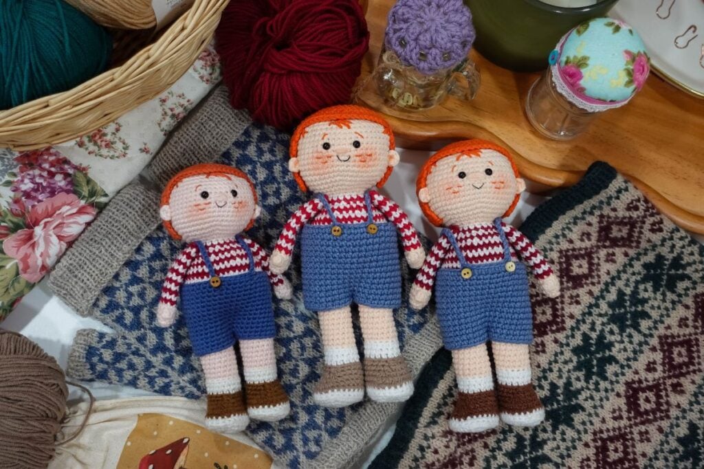 Three handmade Sam Humphrey amigurumi boy dolls with red hair, blue overalls, and red-and-white striped shirts